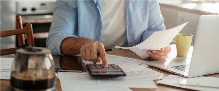 Man using a calculator holding paper in his hand at a desk