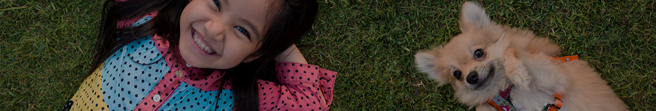 A happy child laying in the grass with a puppy