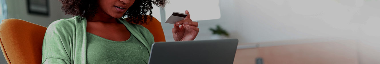 A woman sitting in a chair with her laptop in her lap and a Debit Card in her hand