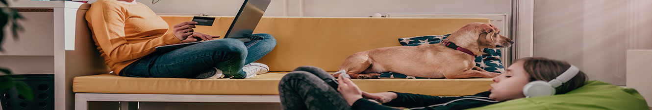 Woman on sofa with a credit card and a laptop sitting next to a dog with a child sitting in a beanbag chair