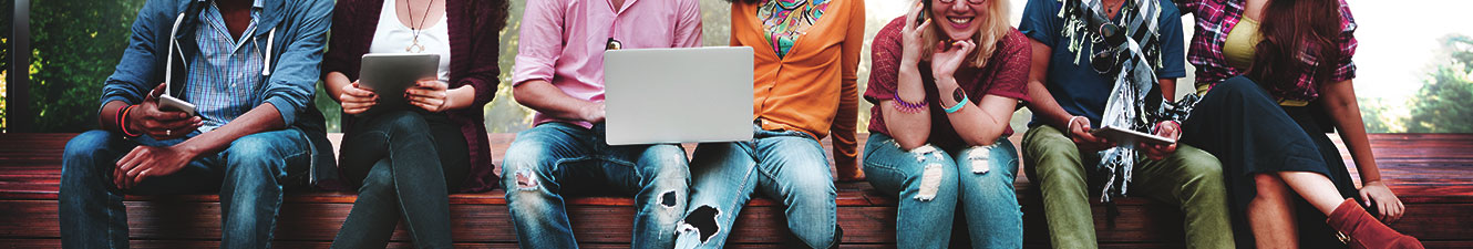 A group of people using various devices such as a cell phone, tablet and laptop while sitting on a bench